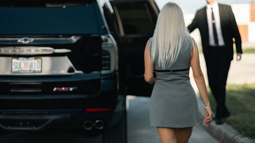 Chauffeur holding the rear door of a black Suburban as a passenger walks to the car