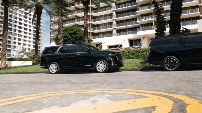 Black Cadillac Escalade parked beneath palm trees outside a high-rise condominium