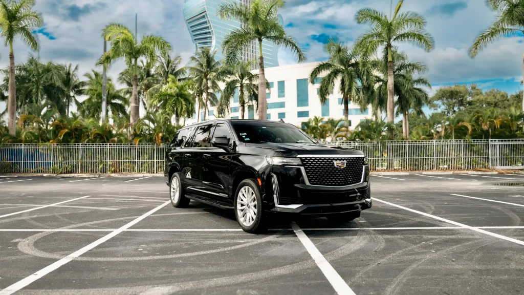 Black Cadillac Escalade parked in front of palm trees and a high-rise