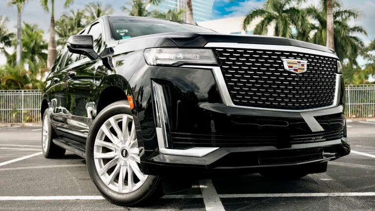 Black Cadillac Escalade premium SUV with chrome grille, parked under palm trees