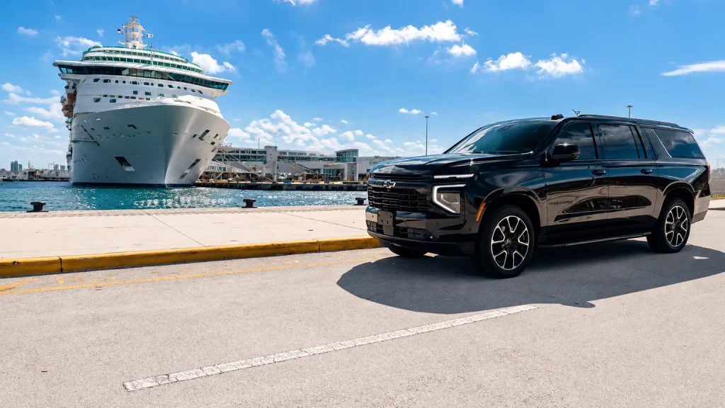 Black Chevrolet Suburban parked on a pier beside a docked cruise ship