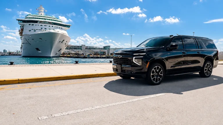 Black Chevrolet Suburban parked on a pier beside a docked cruise ship
