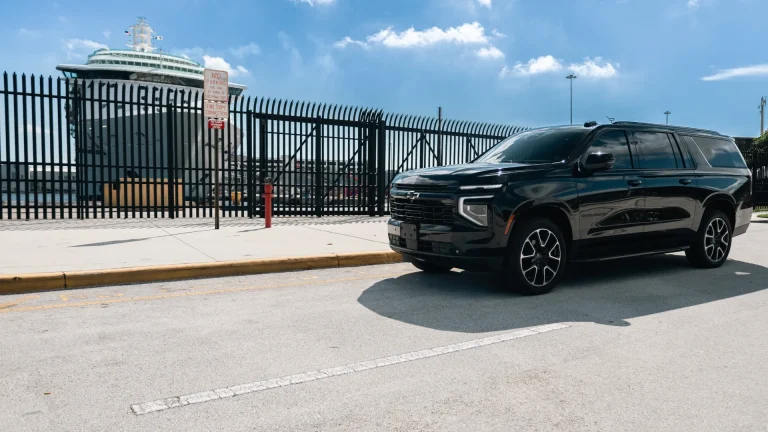 Black Suburban parked by the fence at a cruise terminal with a ship docked behind it