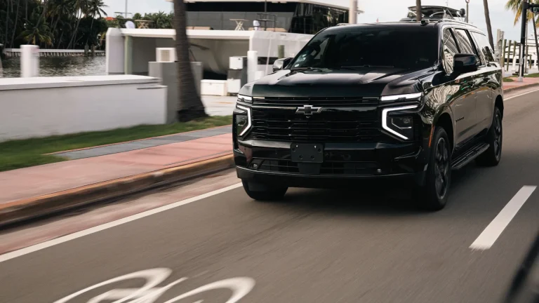 Black Chevrolet Suburban driving past docked yachts on a waterfront road