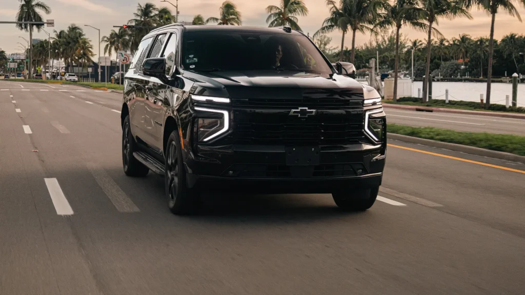 Black Suburban driving on a palm-lined boulevard at dusk
