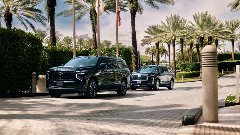 Black Suburban and Escalade waiting at a palm-lined resort entrance