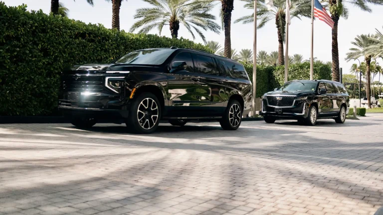 Black Suburban and Escalade at a palm-lined resort entrance