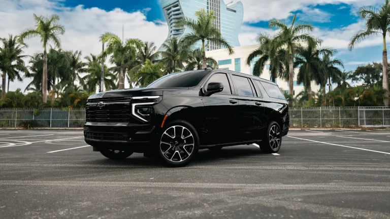 Black Chevrolet Suburban under palm trees with a tall hotel tower behind it