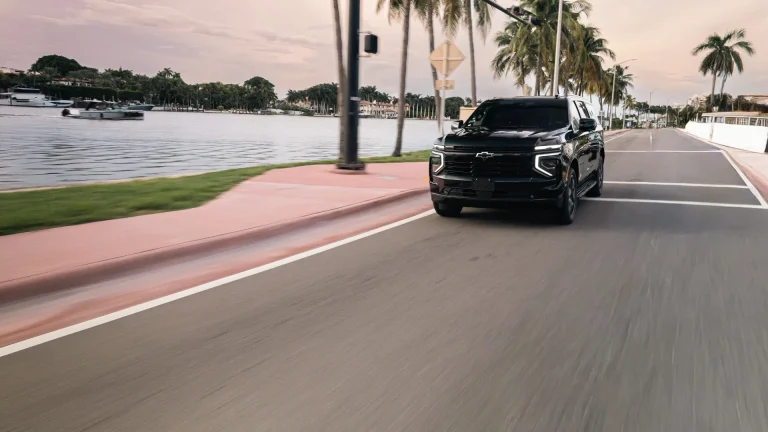 Black Suburban driving along a palm-lined waterfront road